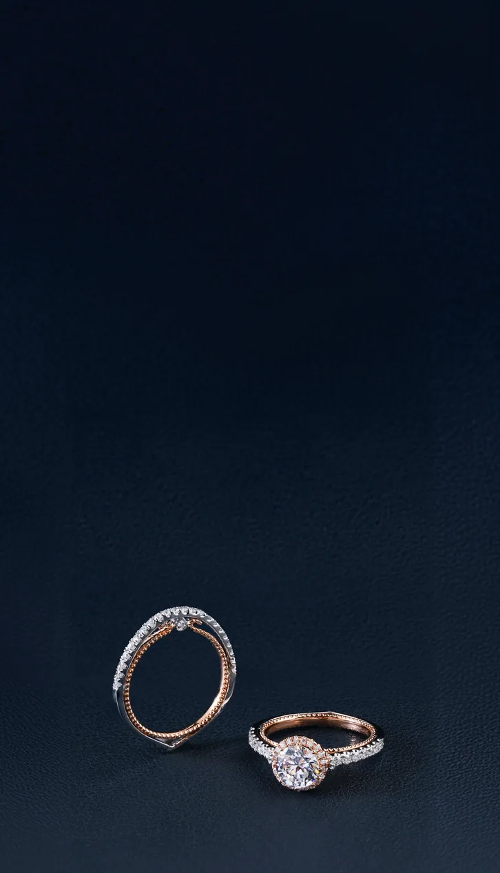 Two diamond engagement rings on a dark textured surface